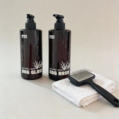 Two black bottles labeled 'Dog Gloss' and 'Dog Wash', a white towel, and a black brush on a light surface.